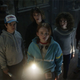 The teenage cast of Netflix's Stranger Things inside an old mansion and staring at something with their flashlights.